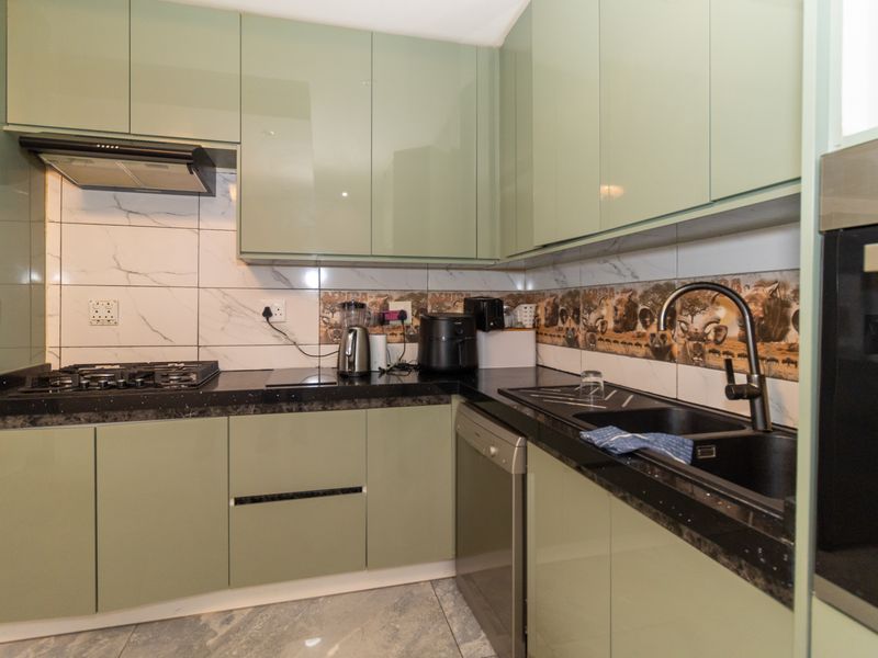 Modern kitchen featuring sage green cabinetry, black granite countertops, integrated gas hob, extractor fan, and a sleek double sink with a contemporary mixer tap.