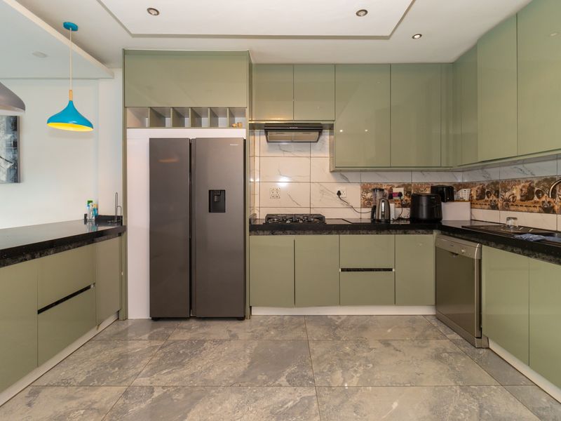 Modern kitchen featuring sage green cabinetry, granite countertops, gas hob, extractor fan, and tiled backsplash with integrated sink and appliance space.