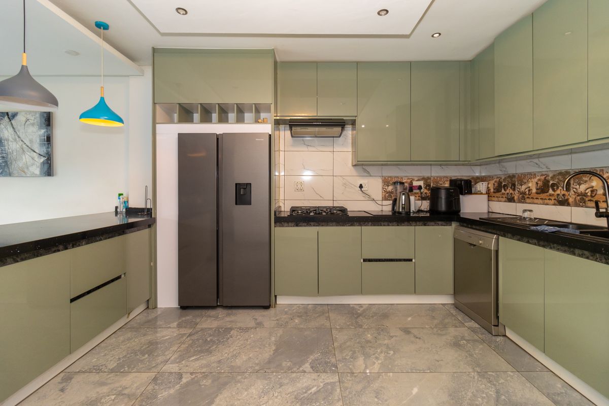 Modern kitchen featuring sage green cabinetry, granite countertops, gas hob, extractor fan, and tiled backsplash with integrated sink and appliance space.