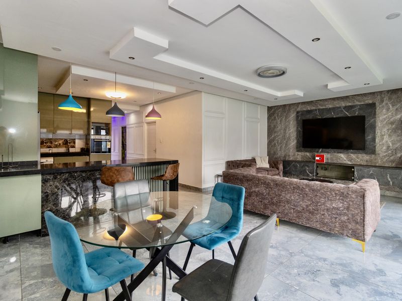 Modern open-plan living area featuring a sleek kitchen with stone countertops, a marble-look feature wall, and contemporary recessed ceiling lighting throughout.