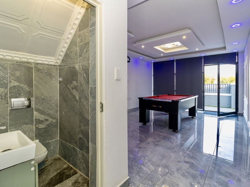 A modern living area featuring polished tiled floors, recessed ceiling lighting, and an adjoining small bathroom with stone wall finishes.