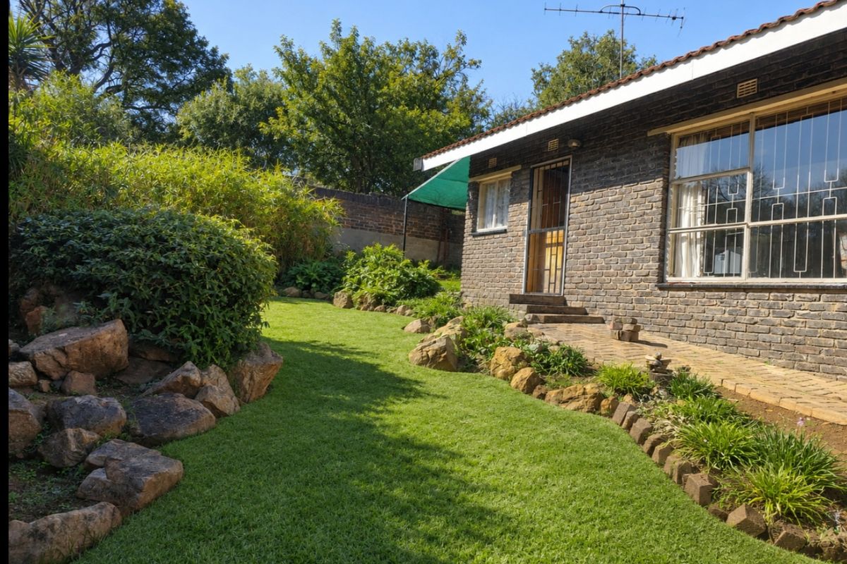 A well-maintained rear garden featuring a brick facade, paved walkway, and established landscaping with rockery elements.