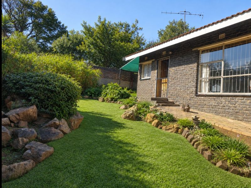 A well-maintained rear garden featuring a brick facade, paved walkway, and established landscaping with rockery elements.
