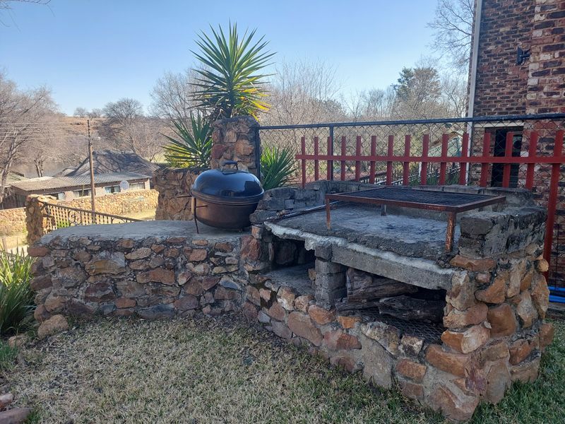 Outdoor entertainment area featuring a rustic stone-built braai and barbecue station, set against a brick exterior wall and metal fencing.