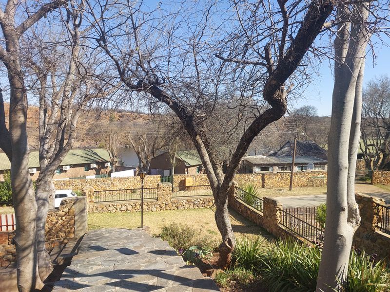 A view of the rear garden area featuring stone boundary walls, wrought iron fencing, and a stone-paved pathway leading through the landscaped yard.