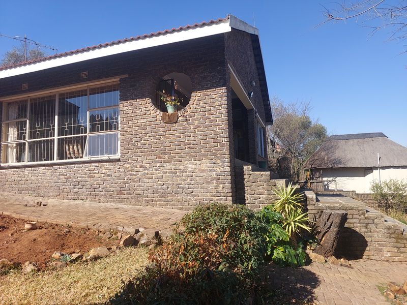 Rear view of a face brick house featuring a tiled roof, security bars on windows, and a paved patio area.