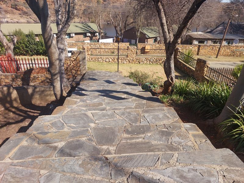 A stone-paved outdoor staircase leading down to a garden area, featuring stone retaining walls and metal perimeter fencing.