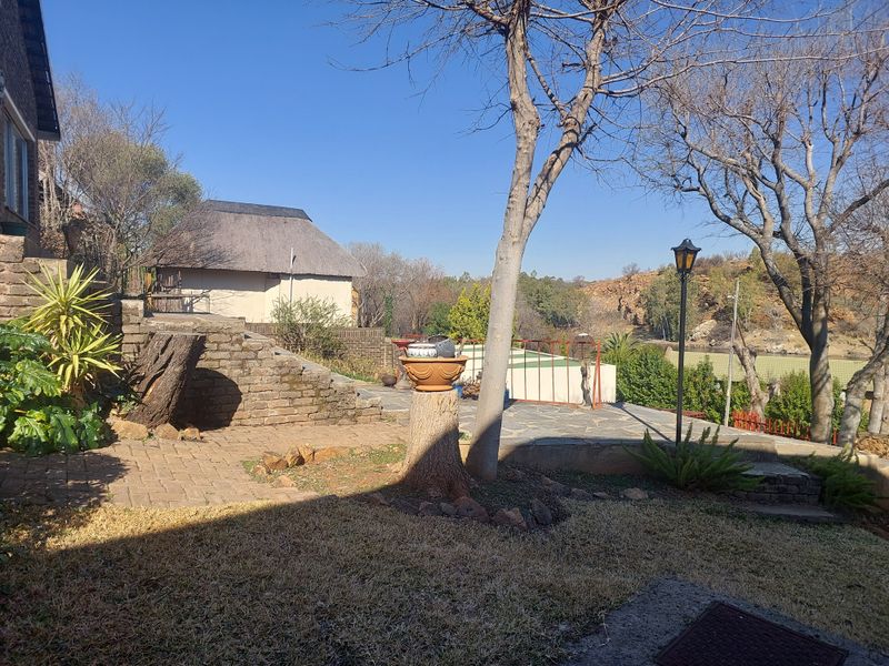 Rear garden area featuring a paved patio, stone retaining walls, and a separate thatched roof structure overlooking the landscape.