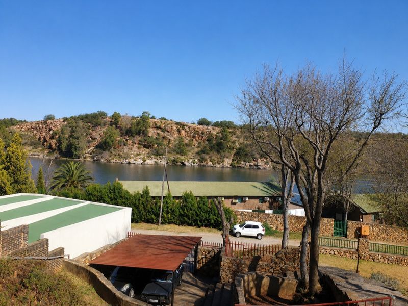 Elevated view overlooking a river with natural rocky terrain, featuring a stone retaining wall and a covered carport area.