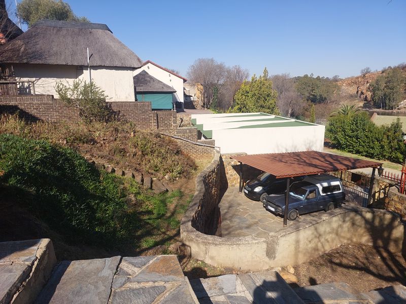 Rear exterior view showing a multi-level garden with stone retaining walls, a paved driveway area, and a covered carport structure.