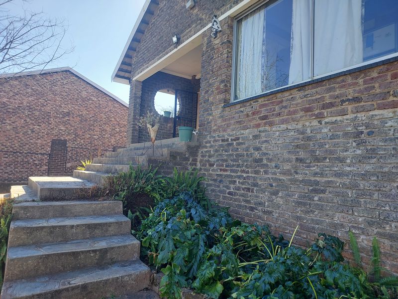 Front elevation of a face brick house featuring a concrete staircase leading to a covered entrance porch and aluminium window frames.
