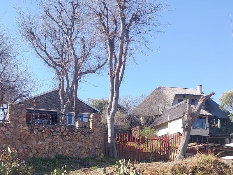 Front elevation view of a property featuring a stone retaining wall, wrought iron fencing, and a multi-level structure with a traditional thatch roof.