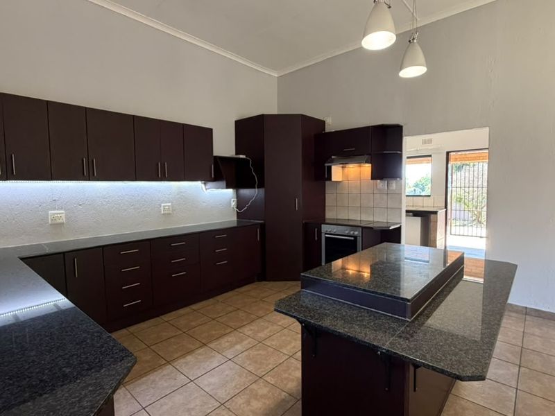 A spacious kitchen featuring dark wood cabinetry, granite countertops, a central island, and tiled flooring, offering a functional layout with integrated appliances.