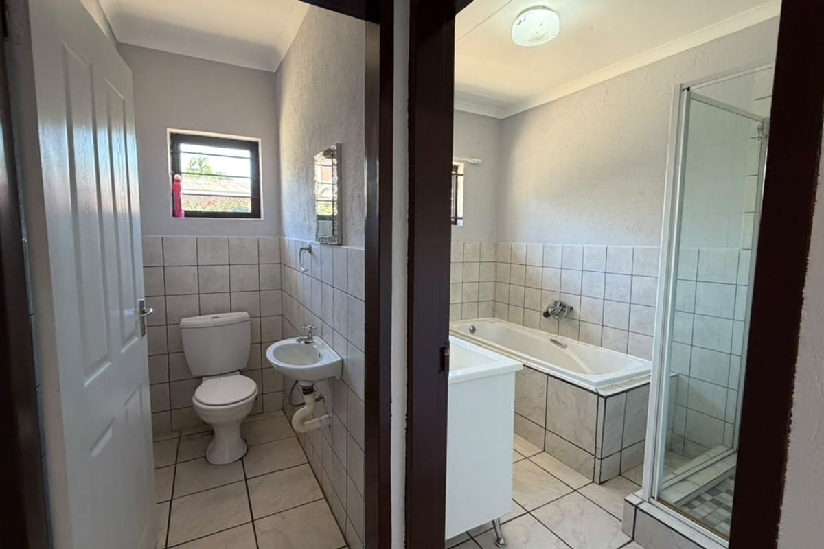 A functional bathroom featuring a separate toilet area, a built-in bathtub, and a glass-enclosed shower with neutral tiled finishes throughout.