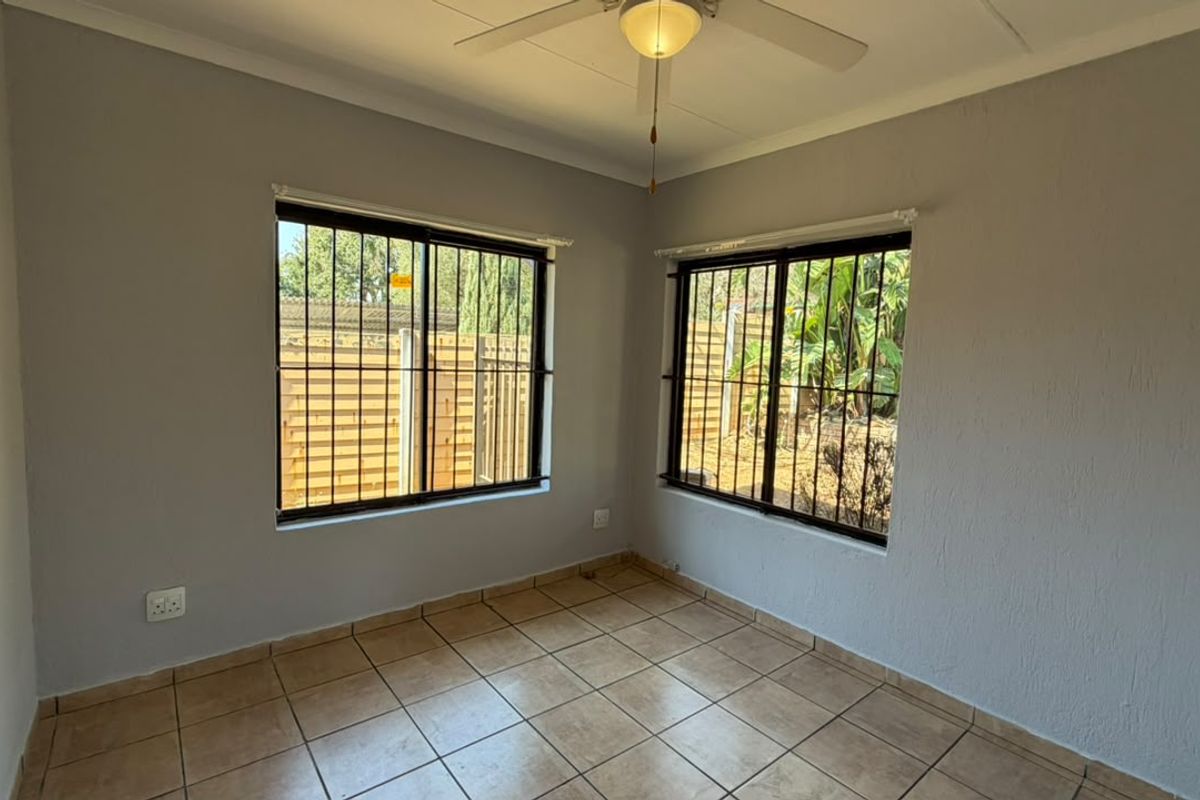 A bright, empty bedroom featuring tiled flooring, a ceiling fan, and windows fitted with security bars, offering a clean canvas for personalization.