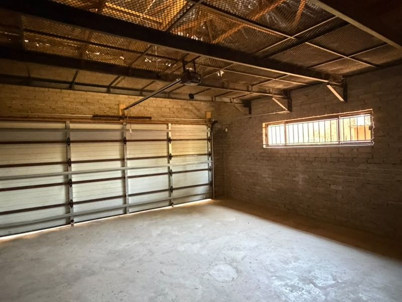 A spacious, unfinished garage featuring exposed brick walls, a metal roof structure, and a functional sectional garage door.