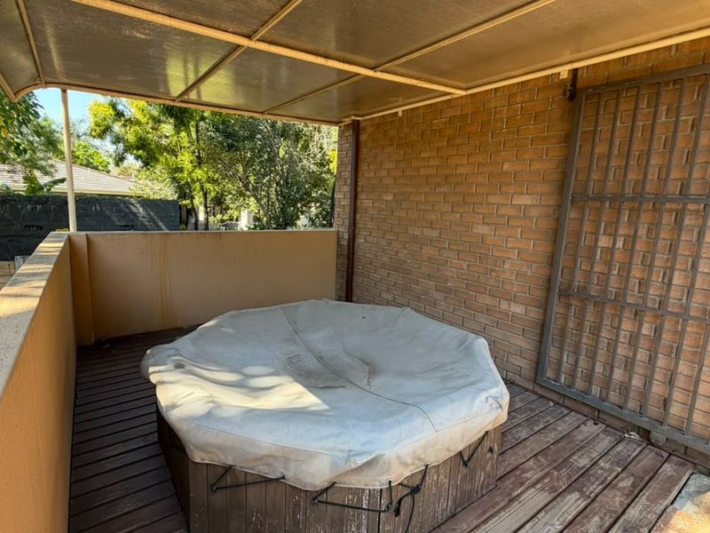 A covered outdoor patio area featuring timber decking, brick wall finishes, and a built-in spa area.
