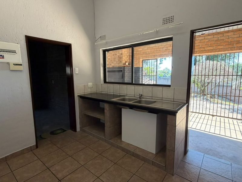 A functional scullery area featuring a double bowl sink, tiled countertops, and direct access to an outdoor patio space.