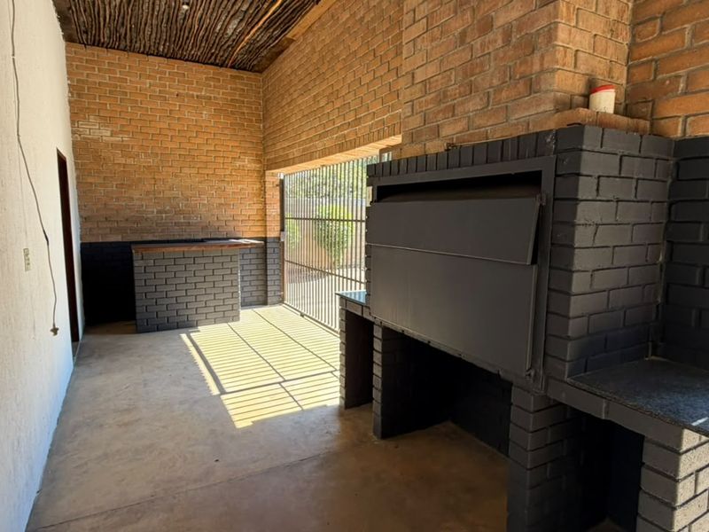 Covered outdoor patio featuring a built-in braai, brick bar counter, and rustic thatched ceiling, ideal for entertaining.