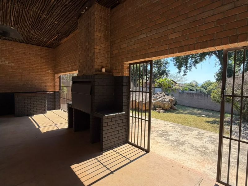 Covered outdoor patio featuring a built-in brick braai, rustic thatched ceiling, and direct access to the garden through security gates.