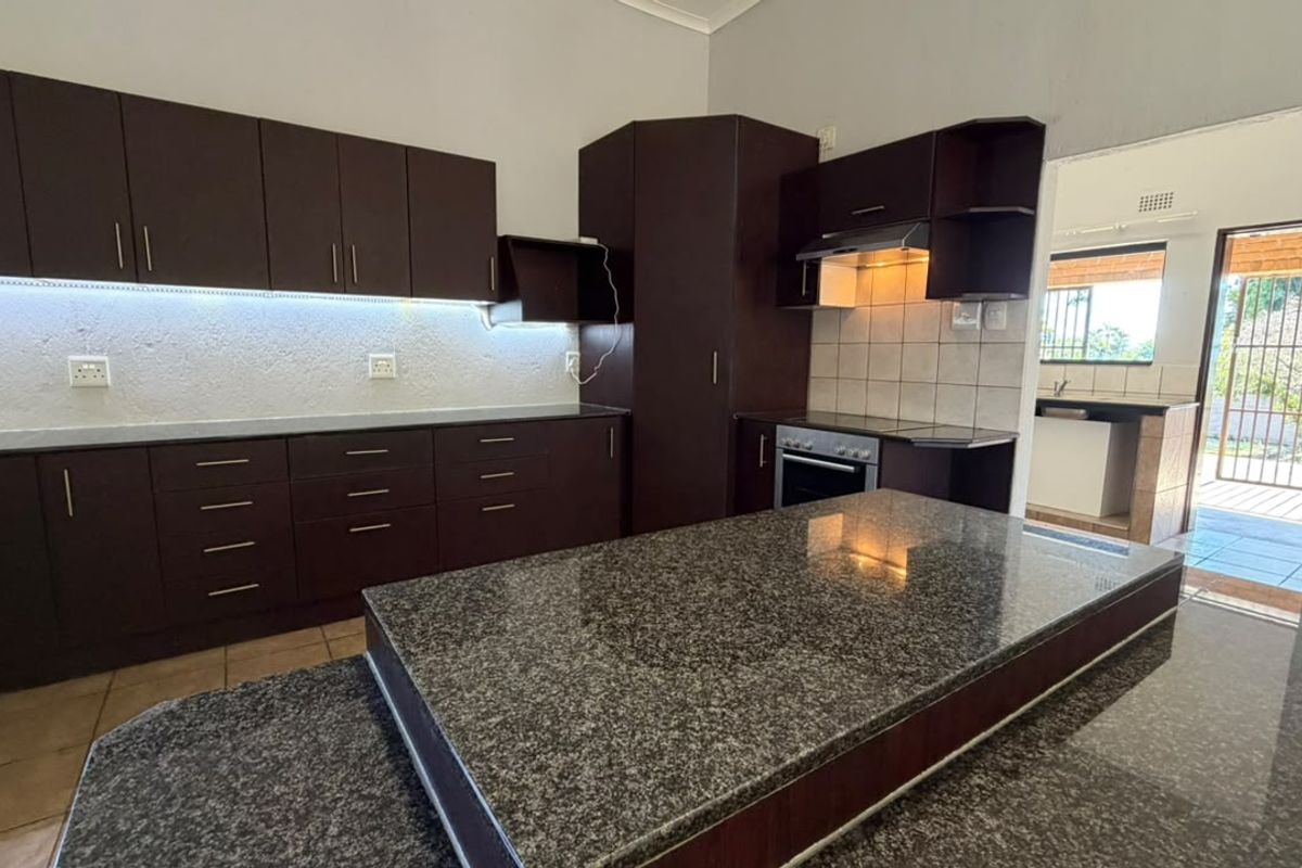 Modern kitchen featuring dark wood cabinetry, granite countertops, a central island, and built-in appliances, with an adjacent scullery area visible.