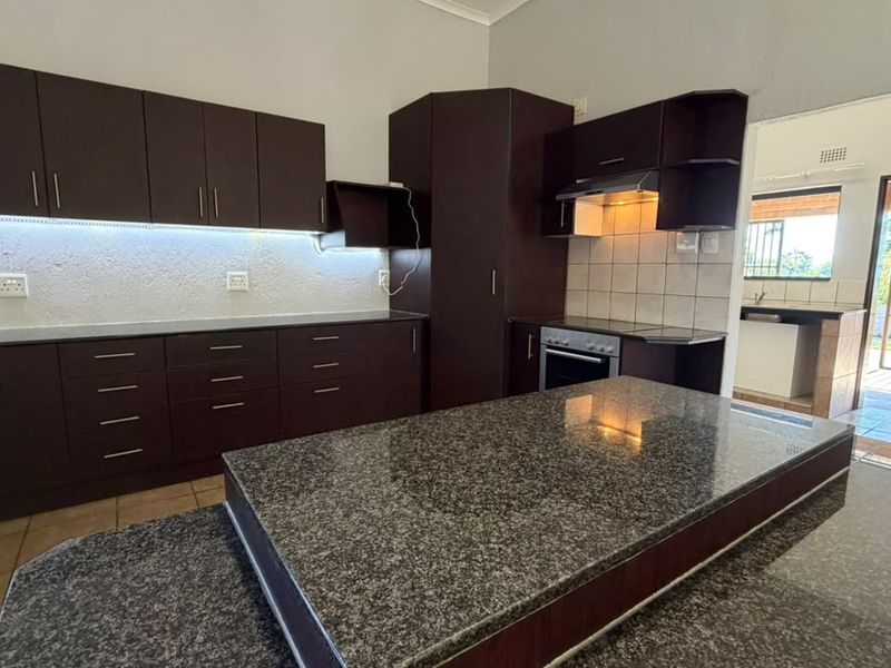 Modern kitchen featuring dark wood cabinetry, granite countertops, a central island, and built-in appliances, with an adjacent scullery area visible.
