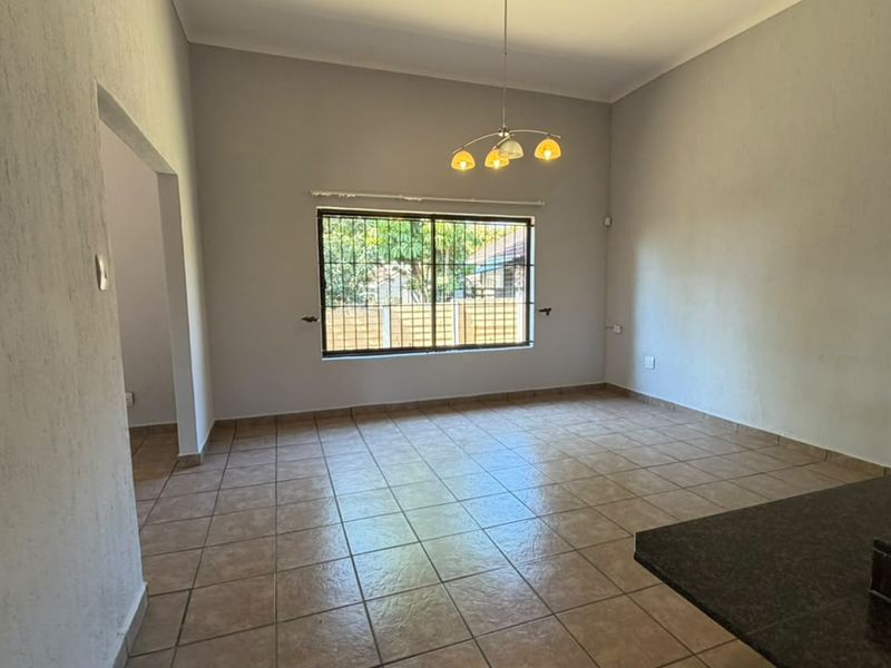 An empty, open-plan living area featuring neutral tiled flooring, a large window with security bars, and a modern pendant light fixture.