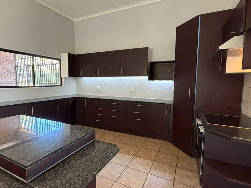 Spacious kitchen featuring dark wood cabinetry, granite countertops, built-in appliances, and tiled flooring with under-cabinet lighting.