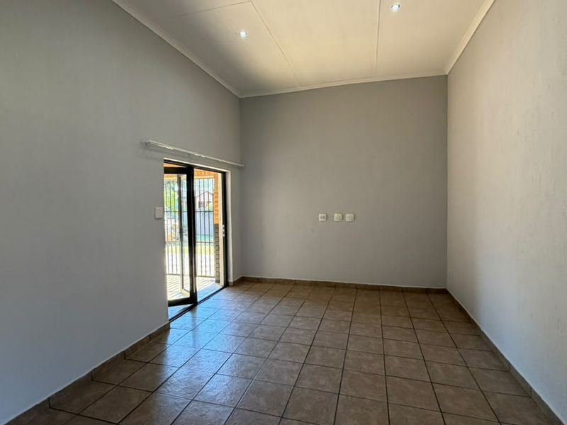 A bright, empty living room featuring neutral walls, tiled flooring, recessed lighting, and a sliding glass door providing access to the exterior.
