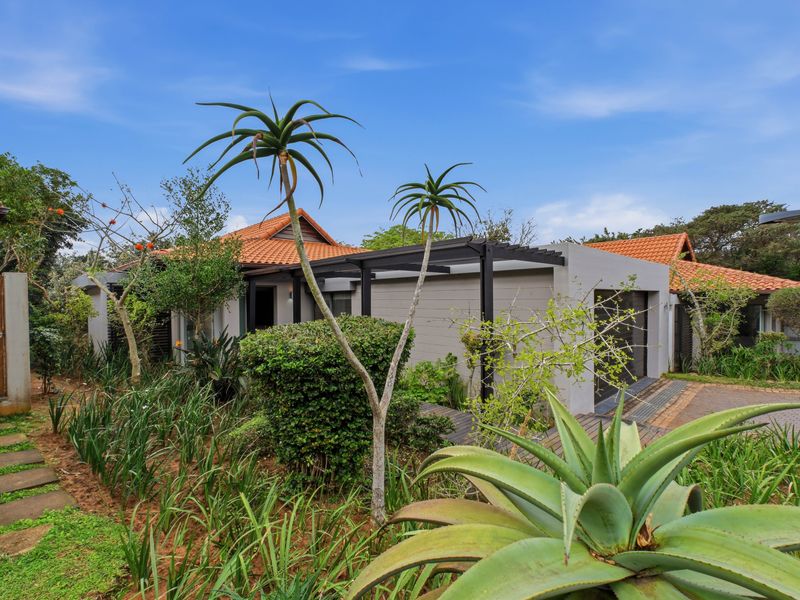 Front exterior view of the townhouse featuring a tiled roof, a modern pergola structure, paved driveway, and established garden landscaping.