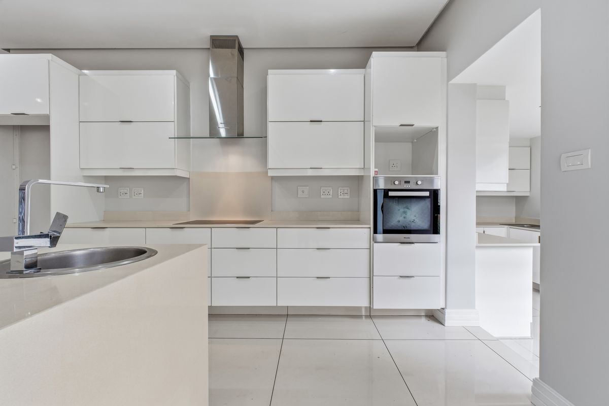 Modern kitchen featuring sleek white gloss cabinetry, stone countertops, integrated oven, extractor fan, and large format floor tiles with a clean, minimalist aesthetic.