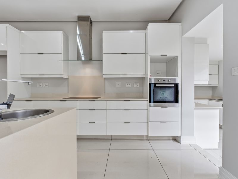 Modern kitchen featuring sleek white gloss cabinetry, stone countertops, integrated oven, extractor fan, and large format floor tiles with a clean, minimalist aesthetic.