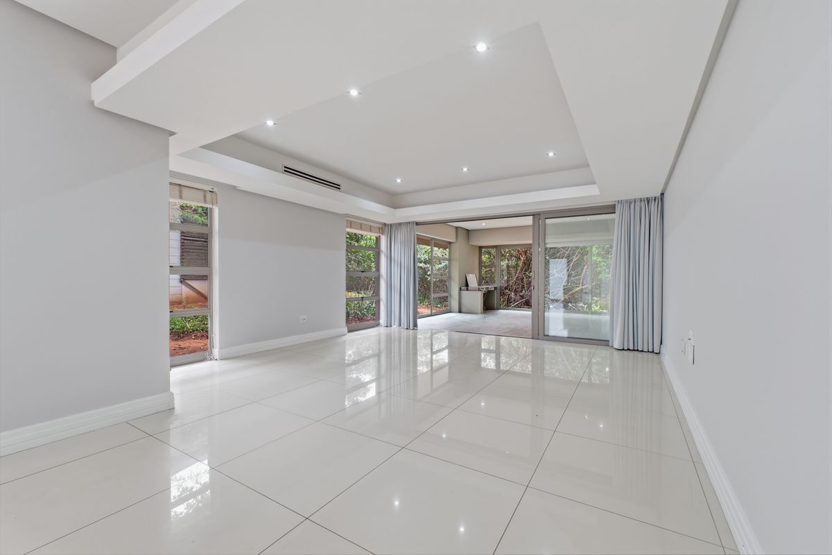 Spacious, modern living area featuring high-gloss tiled floors, recessed ceiling with downlights, ducted air conditioning, and large sliding doors opening to an outdoor space.