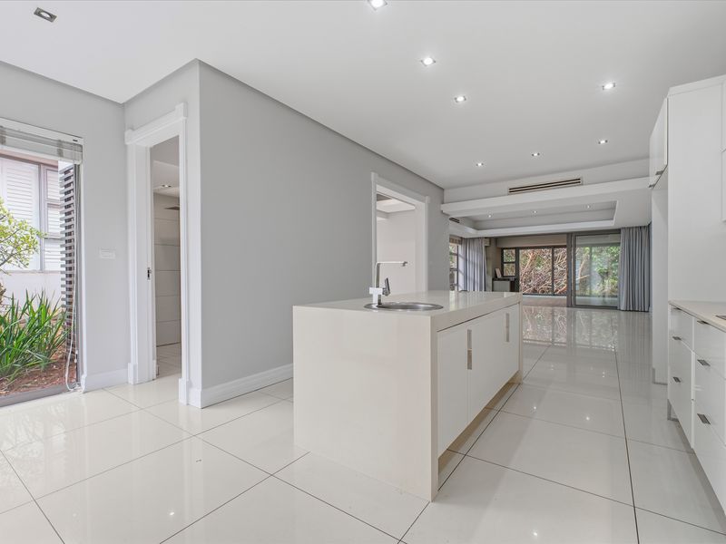 Modern open-plan kitchen featuring a central island, sleek cabinetry, and polished porcelain tiles, flowing seamlessly into the living area with large glass sliding doors.