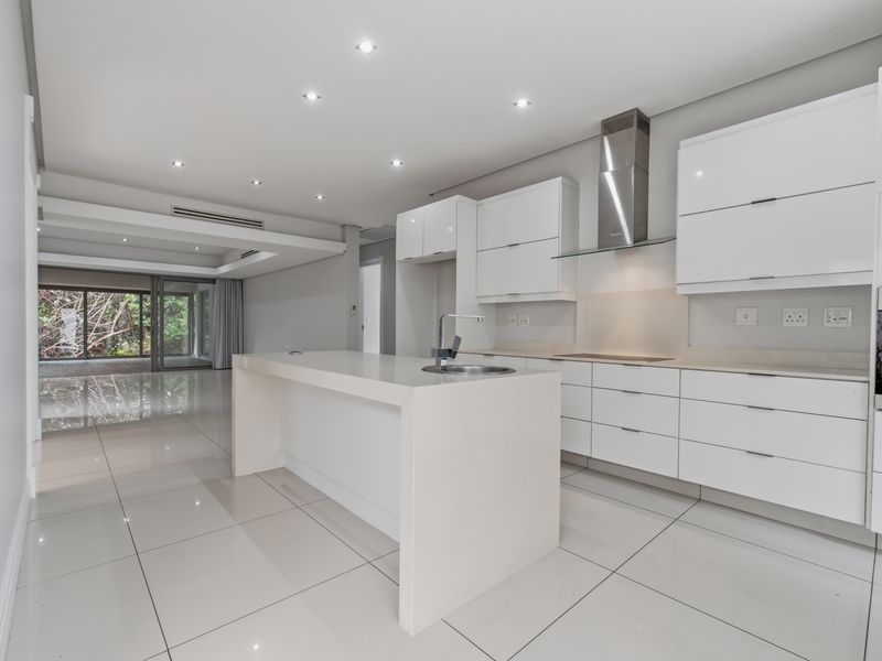 Modern open-plan kitchen featuring sleek white cabinetry, a central island with a sink, and integrated appliances, flowing into a spacious living area.