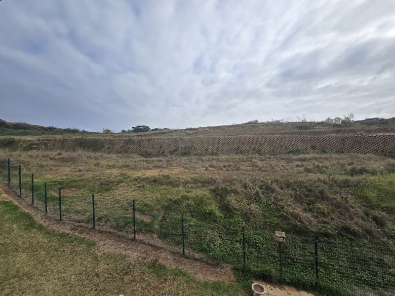 An elevated view of an open, undeveloped plot of land featuring a large retaining wall and perimeter wire fencing.