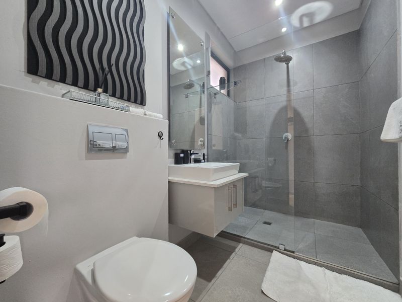 Modern bathroom featuring a wall-hung toilet with concealed cistern, floating vanity with vessel sink, and a spacious walk-in shower with glass screen.