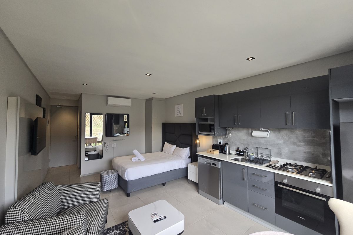Modern open-plan studio apartment featuring a compact kitchen with built-in appliances, tiled flooring, and integrated bedroom area with recessed lighting.