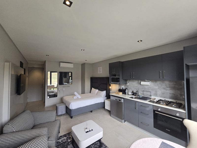 Modern open-plan studio apartment featuring a compact kitchen with built-in appliances, tiled flooring, and integrated bedroom area with recessed lighting.