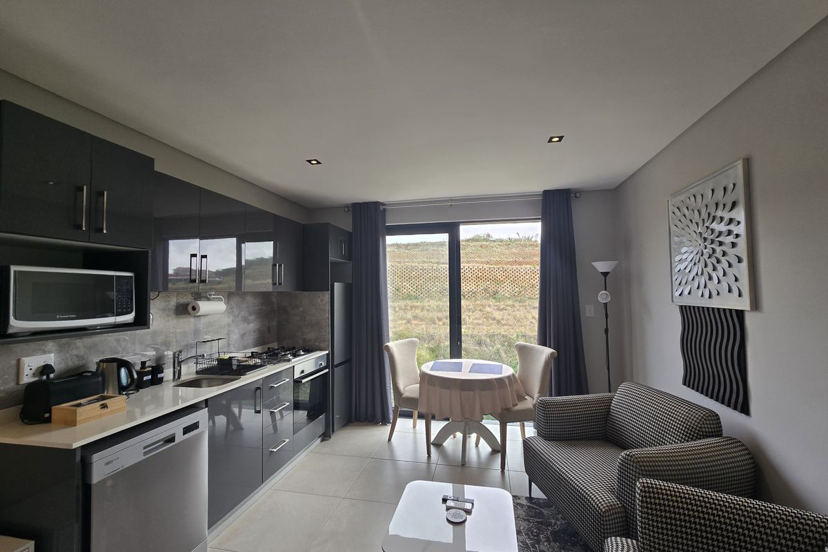 Modern open-plan kitchen and living area featuring high-gloss cabinetry, stone countertops, integrated appliances, and direct access to an outdoor space through sliding doors.