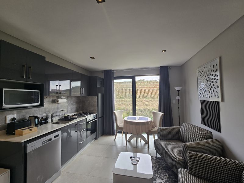 Modern open-plan kitchen and living area featuring high-gloss cabinetry, stone countertops, integrated appliances, and direct access to an outdoor space through sliding doors.