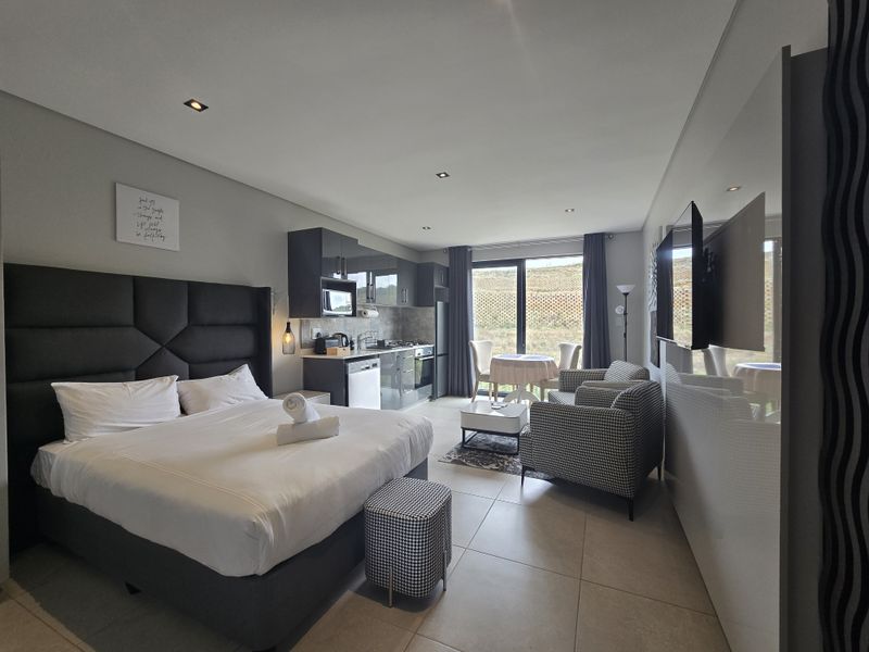 Modern open-plan studio apartment featuring a compact kitchenette with built-in cabinetry, tiled flooring, and large sliding glass doors leading to an outdoor area.