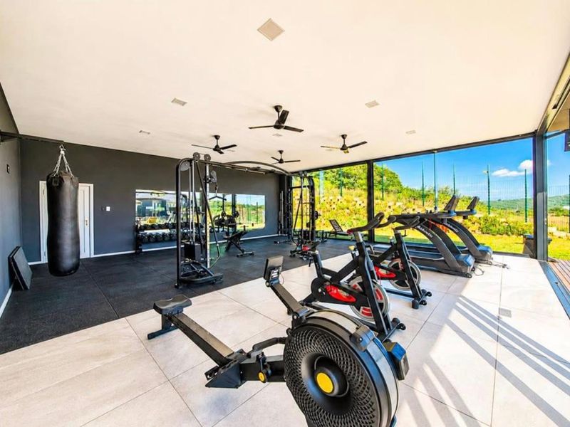 A modern, well-lit gym facility featuring large glass walls, mirrored surfaces, and a combination of tiled and rubber flooring.