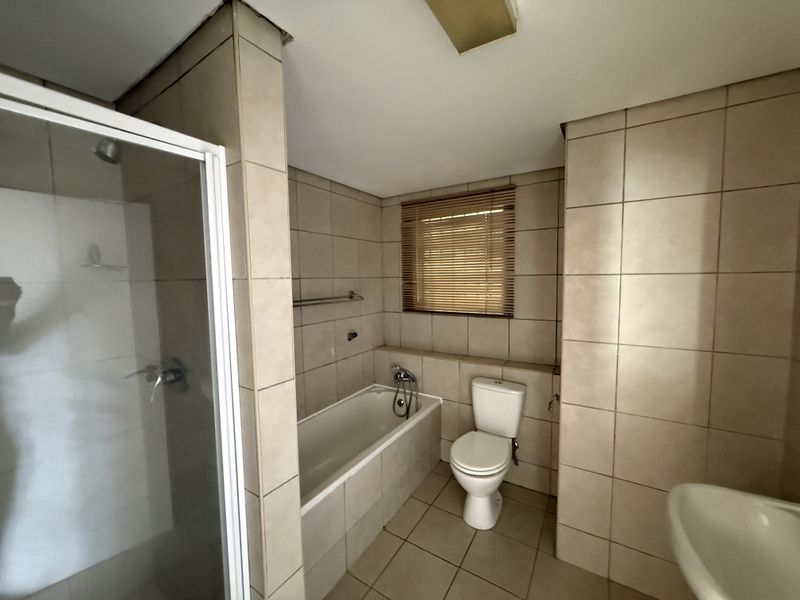 A functional bathroom featuring a shower enclosure, bathtub, toilet, and neutral wall and floor tiling.