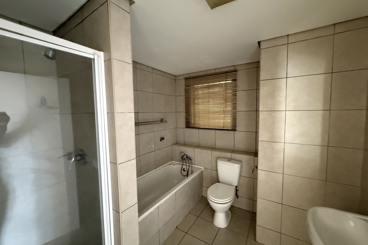 A functional bathroom featuring a shower enclosure, bathtub, toilet, and neutral wall and floor tiling.