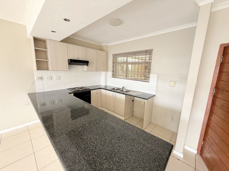 A functional kitchen featuring granite countertops, built-in cabinetry, an electric hob, oven, extractor fan, and a double bowl sink with tiled flooring.