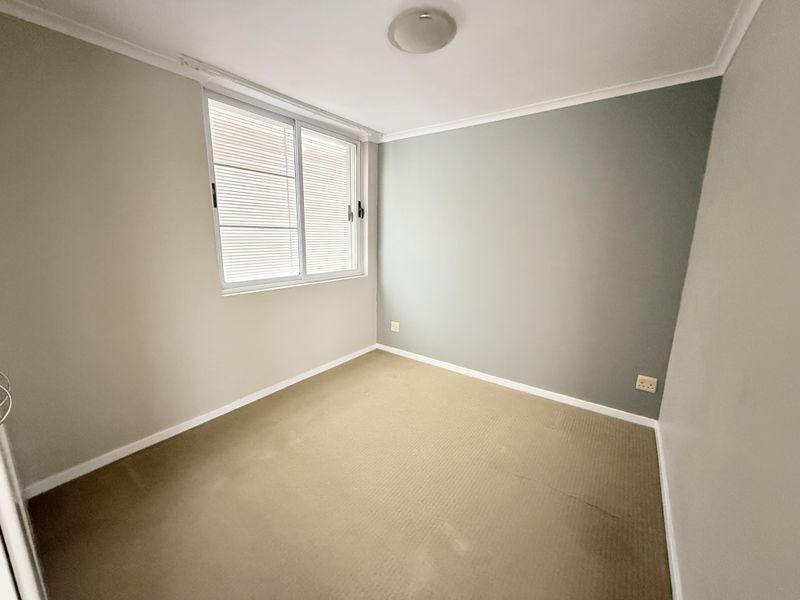 A vacant bedroom featuring neutral wall tones, a feature wall, carpeted flooring, and a sliding window with integrated blinds.