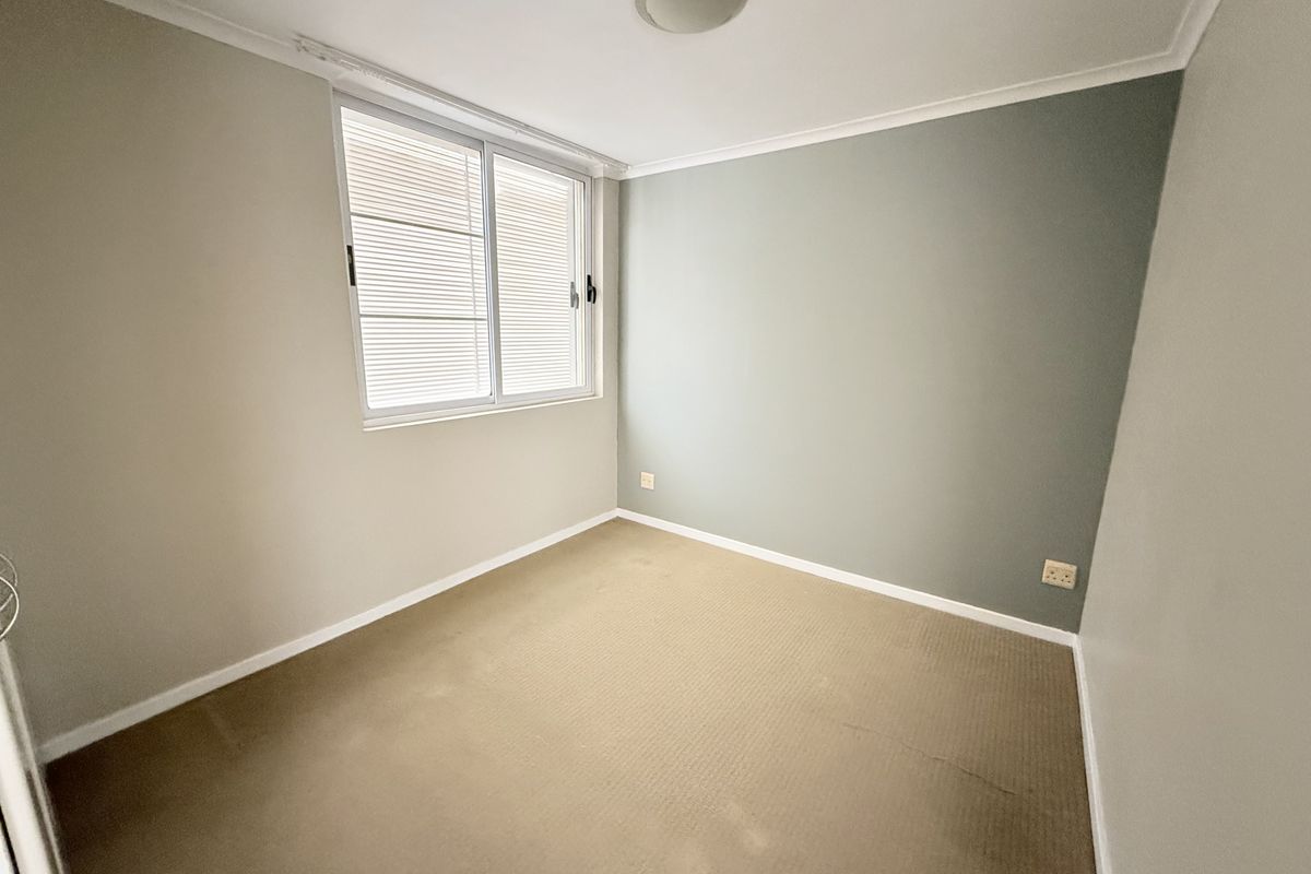 A vacant bedroom featuring neutral wall tones, a feature wall, carpeted flooring, and a sliding window with integrated blinds.