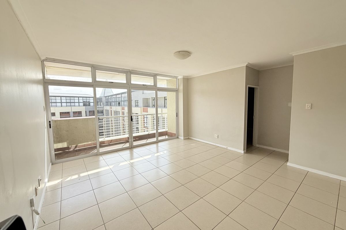 A bright, empty living room featuring neutral tiled flooring and large sliding glass doors that provide access to an attached balcony.