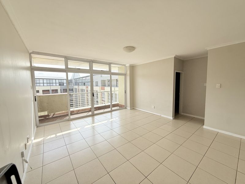 A bright, empty living room featuring neutral tiled flooring and large sliding glass doors that provide access to an attached balcony.